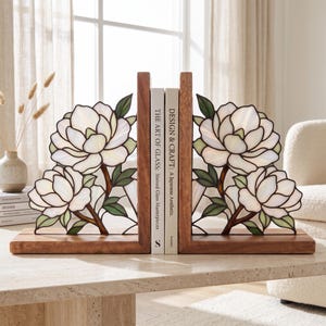 May include: A pair of wooden bookends featuring stained glass panels with white magnolia flowers and green leaves. The bookends hold two books titled The Art of Glass: Stained Glass Masterpieces and Design & Craft: A Japanese Aesthetic.
