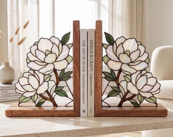 May include: A pair of L-shaped wooden bookends featuring stained glass panels with white magnolia flowers and green leaves. The bookends hold two books titled The Art of Glass: Stained Glass Masterpieces and Design & Craft: A Japanese Aesthetic.