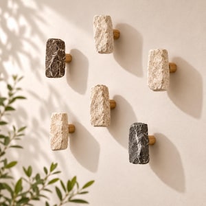 Peut inclure: Un ensemble de six patères murales, chacune dotée d'une façade en pierre naturelle brute dans des tons gris foncé et beige clair, fixée sur une base métallique cylindrique de couleur laiton. Les patères sont disposées de manière éparse.