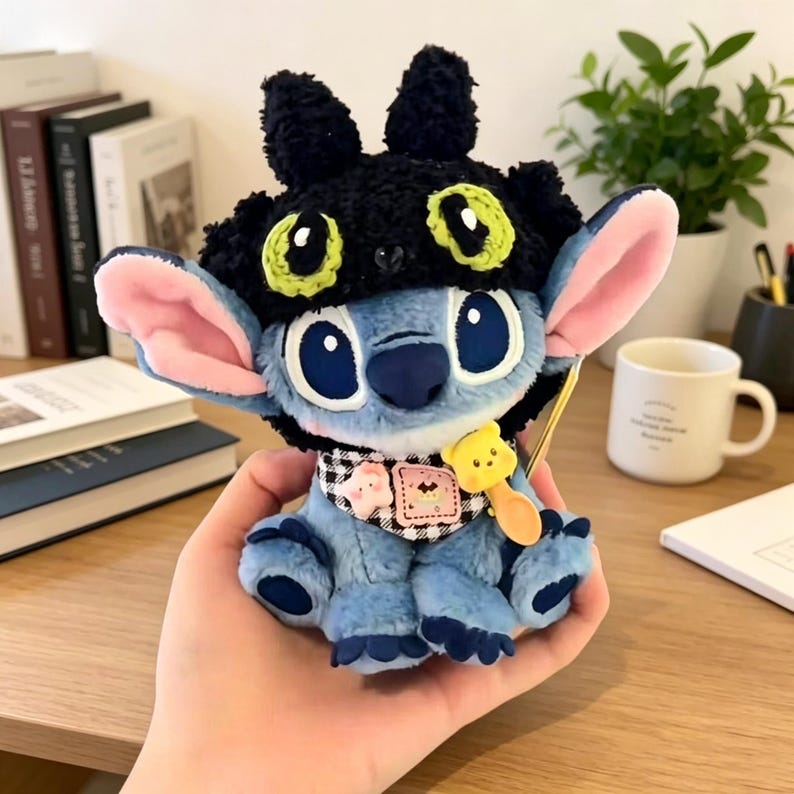 May include: A blue plush character toy wearing a black textured hat with green and black eye patterns. The toy features large pink-lined ears, a black and white checkered neck scarf with small star and bear charms, and a yellow spoon accessory.