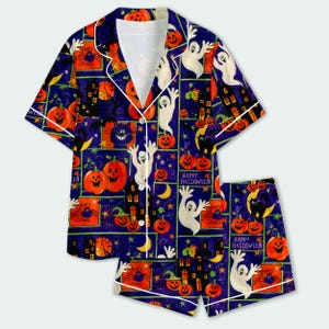 Pode incluir: Um conjunto de pijama com camisa de manga curta abotoada e calções a condizer em tecido azul escuro, apresentando um padrão repetitivo de Halloween com abóboras cor de laranja, fantasmas brancos, gatos pretos e casas assombradas.