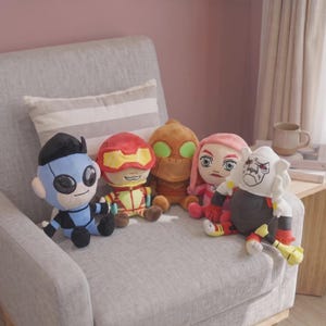 May include: A collection of five plush toys featuring diverse characters. The group includes a blue figure with black hair, a red character with yellow goggles, a brown textured figure, a pink-haired character, and a white-furred figure in armour.