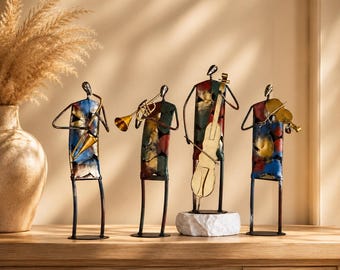 Puede incluir: Un conjunto de cuatro figuras de músicos de metal con cuerpos abstractos en tonos azul, rojo y dorado. Las figuras incluyen un saxofonista, un trompetista, un violonchelista sobre una base de piedra blanca y un violinista, todos de pie.