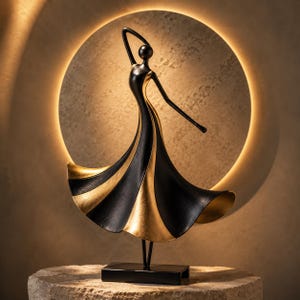 May include: A decorative sculpture of a dancing figure with a stylised, elongated form. The figure features a flowing dress with alternating panels of matte black and metallic gold finish, standing on a rectangular black base.
