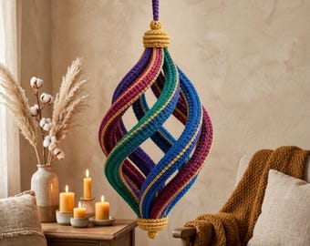 Puede incluir: Un adorno de ganchillo colgante con un diseño en espiral en forma de lágrima. La estructura se compone de bandas verticales alternas en morado intenso, verde azulado y azul real, acentuadas con un borde fino y una tapa de color amarillo.
