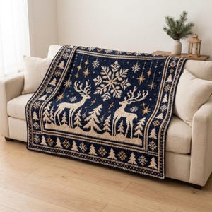 Op de afbeelding: Een rechthoekige plaid met een donkerblauwe achtergrond en een crèmekleurig patroon van twee herten, dennenbomen, grote sneeuwvlokken en kleine sterren. De rand bevat een herhalend ontwerp van kleine dennenbomen en sneeuwvlokken.