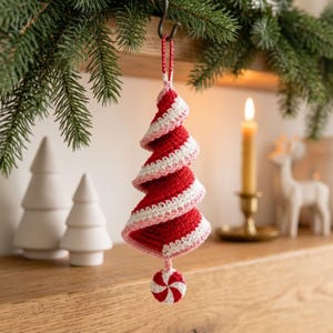 May include: A spiral-shaped Christmas tree ornament made of red and white crocheted yarn. The ornament features a candy cane-inspired color pattern and hangs from a small loop. A round, red and white peppermint-style crocheted disc is attached to the bottom.