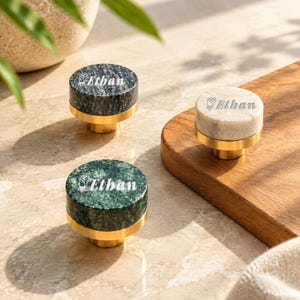 May include: Three cylindrical cabinet knobs with gold-toned metal bases and circular stone tops in black, white, and green marble. Each knob features the engraved name Ethan accompanied by a small rose icon on the top surface of the stone.