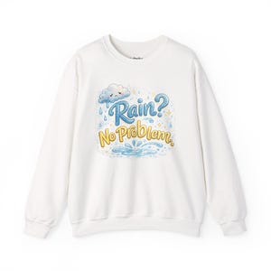 May include: A white long-sleeve crewneck sweatshirt featuring a central graphic illustration of a sad grey cloud with blue raindrops. The text reads "Rain? No Problem." in blue and yellow script, accompanied by small yellow stars and a blue puddle.