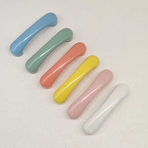 May include: A set of six arched cabinet handles in a smooth, glossy finish. The handles are arranged diagonally and feature a variety of solid colours including light blue, sage green, coral, bright yellow, soft pink, and off-white.