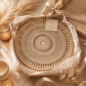 May include: A round, cream-colored macrame wall hanging with intricate knotted patterns and a fringed edge. A square tag attached to the top reads "HANDMADE WITH LOVE just for you". The item is nestled in tissue paper inside a gift box with a ribbon.