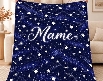 May include: A dark blue fleece blanket featuring a white celestial pattern of stars and shooting stars across the entire surface. The name Mame is printed in the center in a large, white, cursive script font with a glowing effect.