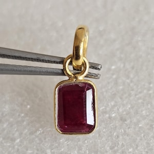 May include: A rectangular, deep red gemstone pendant set in a polished yellow gold bezel. The pendant features a small, circular gold jump ring at the top, designed for attachment to a chain, showcasing a classic, clean-lined jewelry design.