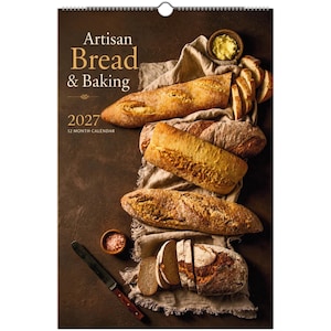Könnte beinhalten: Ein Wandkalender für 2027 mit dem Titel Artisan Bread & Baking, der verschiedene Brote auf einem beigen Tuch, eine kleine Schale mit Butter, eine kleine Schale mit rosa Salz und ein Messer auf einer dunkelbraunen Oberfläche zeigt.