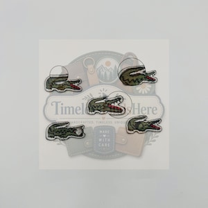 Può includere: Cinque toppe ricamate a forma di coccodrilli verdi con denti bianchi e bocche rosse. Ogni toppa presenta una trama cucita dettagliata. Le toppe sono disposte su uno sfondo bianco con un logo contenente il testo Timeless Finds Here.