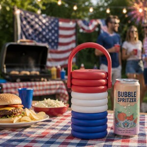 May include: A stackable red, white, and blue plastic beverage cooler with a handle, positioned next to a 12-ounce can of Bubble Spritzer sparkling beverage, a cheeseburger on a plate, and a bowl of coleslaw on a checkered tablecloth.