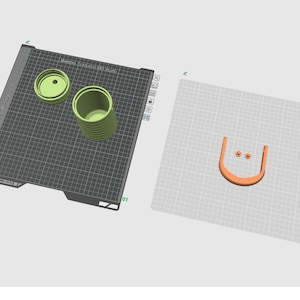 May include: A digital 3D modeling interface displaying two distinct build plates. The first plate features a light green cylindrical container and a matching lid. The second plate shows an orange U-shaped component and two small circular orange pieces.