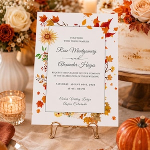 Peut inclure: Une carte d'invitation de mariage rectangulaire avec une bordure de feuilles d'automne et de fleurs à l'aquarelle. Le texte indique : Together with their families, Rose Montgomery and Alexander Hayes, request the pleasure of your company at the celebration of their wedding, Saturday, August 01st, 2026 at 04:00 PM, Cedar Valley Lodge, Aspen Colorado.
