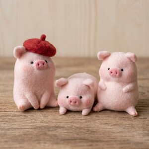 May include: Three needle-felted pig figurines made of soft pink wool. The pig on the left wears a small, textured dark red beret. Each pig features tiny black bead eyes, a rounded snout, and small ears. They are positioned in a row on a surface.