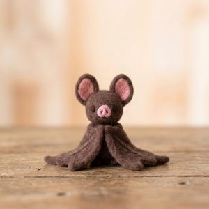 Peut inclure: Une petite figurine de chauve-souris en laine feutrée à l'aiguille de couleur brun foncé. La chauve-souris possède deux grandes oreilles arrondies avec des détails intérieurs rose pâle, un petit museau rose et deux minuscules yeux noirs.