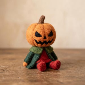 Könnte beinhalten: Eine nadelgefilzte Kürbisfigur mit einem geschnitzten Jack-o'-Lantern-Gesicht, schwarzen Augen und einem gezackten Mund. Die Figur trägt einen dunkelgrünen Mantel mit breitem Kragen über einem roten Hemd und hat kleine rote Füße.
