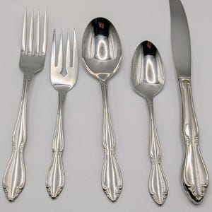 May include: A set of five silver-colored flatware pieces, including a fork, a salad fork, two spoons, and a knife. The utensils have a decorative floral design on the handles. The knife blade is approximately 8 inches long.