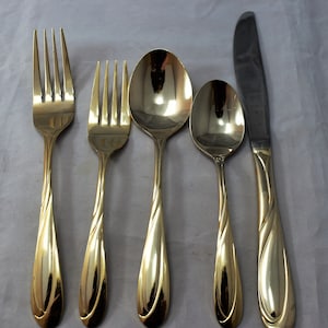 May include: A set of five gold-plated flatware pieces, including a fork, knife, and three spoons. The flatware has a twisted design and a polished finish.