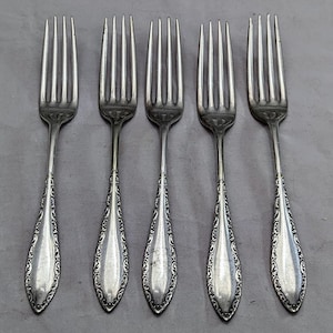 May include: Five silver forks with ornate designs on the handles.