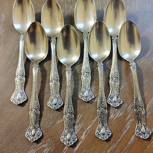 May include: A set of ten silver teaspoons with ornate handles featuring a grapevine design. The spoons are polished and have a vintage look.