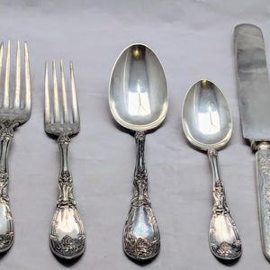 May include: Set of five silver-plated flatware pieces, including a fork, a knife, and three spoons. The pieces have ornate designs and are in excellent condition.