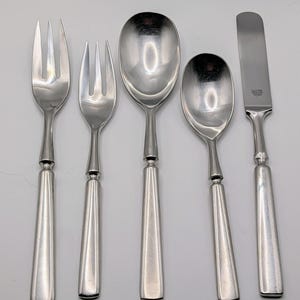 May include: A set of silver-colored flatware, including two forks, two spoons, and a butter knife. The utensils have a simple, elegant design with tapered handles. The butter knife has the word "Dansk" printed on it.