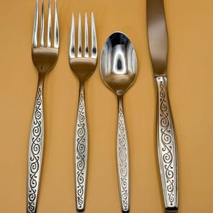 May include: A set of silverware with a decorative swirl pattern on the handles. The set includes a fork, a knife, and a spoon.