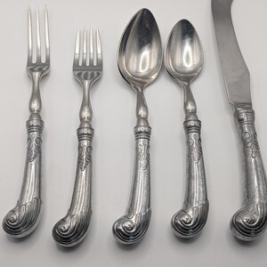May include: A set of antique silverware, including two forks, two spoons, and a butter knife. The silverware has ornate, curved handles with a detailed floral design. The metal has a silver finish.