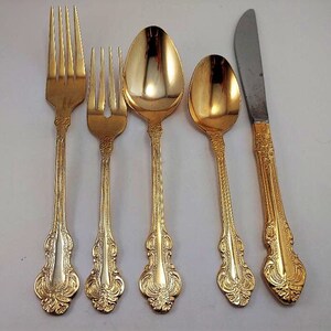 May include: Set of five gold-plated silverware pieces, including a knife, fork, and three spoons. The silverware has an ornate design with a gold finish.