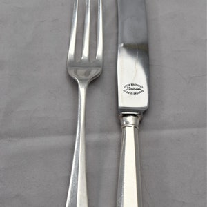 May include: A silver fork and knife set. The fork has three tines and a teardrop-shaped handle. The knife has a curved blade and a handle with a rounded end. The knife is stamped with "ATKIN BROTHERS Stainless MADE IN ENGLAND."