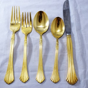 May include: A set of gold-plated silverware, including a fork, knife, and two spoons. The silverware has a decorative, fluted design on the handles.