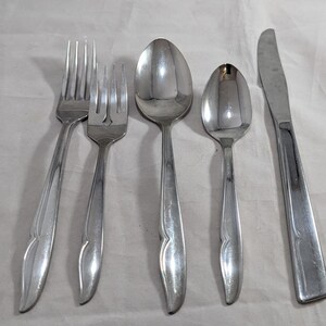 May include: Set of five silver-toned flatware pieces, including two forks, two spoons, and a butter knife. The handles of each piece have a decorative, curved design.