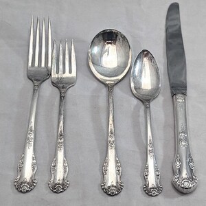 May include: Set of five silver-plated flatware pieces, including a fork, knife, and three spoons. The pieces have ornate floral designs.