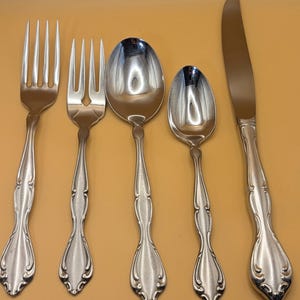 May include: A set of five silver-plated flatware pieces, including a fork, a knife, and three spoons. The flatware has an ornate, decorative design.