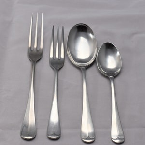May include: Four pieces of silverware, including two forks and two spoons, are arranged on a white tablecloth. The silverware is made of polished metal and has a simple, elegant design.