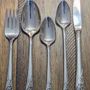May include: Set of five silver-plated flatware pieces with ornate floral designs on the handles. The set includes a fork, two spoons, and a butter knife.