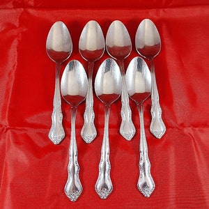 May include: Set of eight silver spoons with ornate handles. The spoons are arranged in a fan shape on a red background.