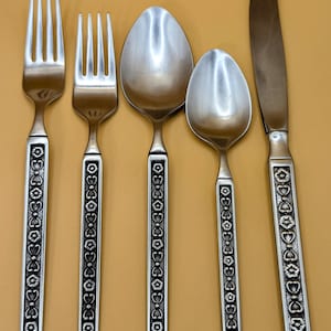 May include: Set of five silver-toned flatware with black floral patterned handles. The set includes a knife, fork, spoon, and two teaspoons.