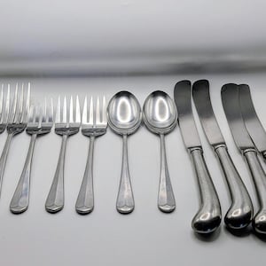 May include: A collection of silver-colored flatware, including forks, spoons, and knives, arranged on a white surface. The forks have four tines, the spoons are oval, and the knives have curved blades. The silverware is likely for dining.