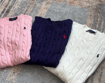Può includere: Tre maglioni a trecce in rosa chiaro, blu navy e bianco. Ogni maglione a maniche lunghe con girocollo presenta colletto e polsini a coste, con un piccolo logo Polo Ralph Lauren ricamato sul petto e un'etichetta del marchio all'interno del collo.