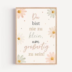 Pode incluir: Um quadro retangular com moldura de madeira clara apresentando o texto em alemão Du bist nie zu klein, um großartig zu sein! rodeado por ilustrações em aguarela de margaridas em tons de rosa suave, branco e verde suave sobre fundo creme.