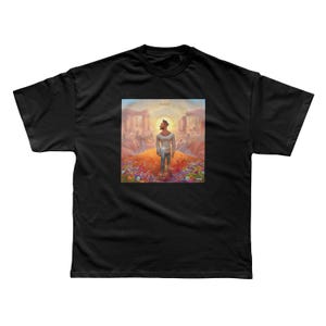 以下が含まれることがあります： 黒の半袖Tシャツ。中央に、輝く太陽、色とりどりの花、岩層が描かれた鮮やかでシュールな風景の中に立つ人物のグラフィックプリントがあり、アートワークの上部には「ALMA」という文字が見えます。