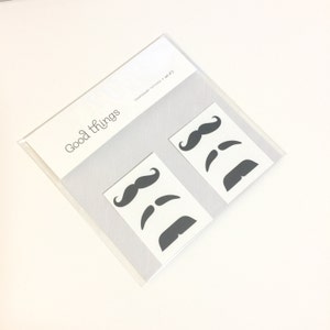 2-sheet set of finger mustache temporary tattoos featuring 6 unique black mustache styles including handlebar, chevron, and pencil stache designs. Hilarious and fun fake tattoos perfect for photo booths, parties, Halloween, Movember, gag gifts, or bachelorette fun. A bestselling classic that brings instant laughs. Easy to apply, safe on skin, and sized to sit right above your finger for that perfect faux-stache moment.