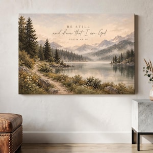 Puede incluir: Un lienzo rectangular de arte mural con una pintura de paisaje de un lago tranquilo rodeado de pinos, flores silvestres y montañas lejanas. El texto BE STILL and know that I am God PSALM 46:10 está impreso en el centro en letras oscuras.