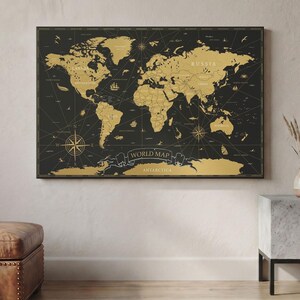 Può includere: Un'opera d'arte da parete rettangolare che raffigura una mappa del mondo con continenti e masse terrestri color oro su uno sfondo nero solido. La mappa include rose dei venti nautiche, illustrazioni di navi e creature marine e il testo WORLD MAP.